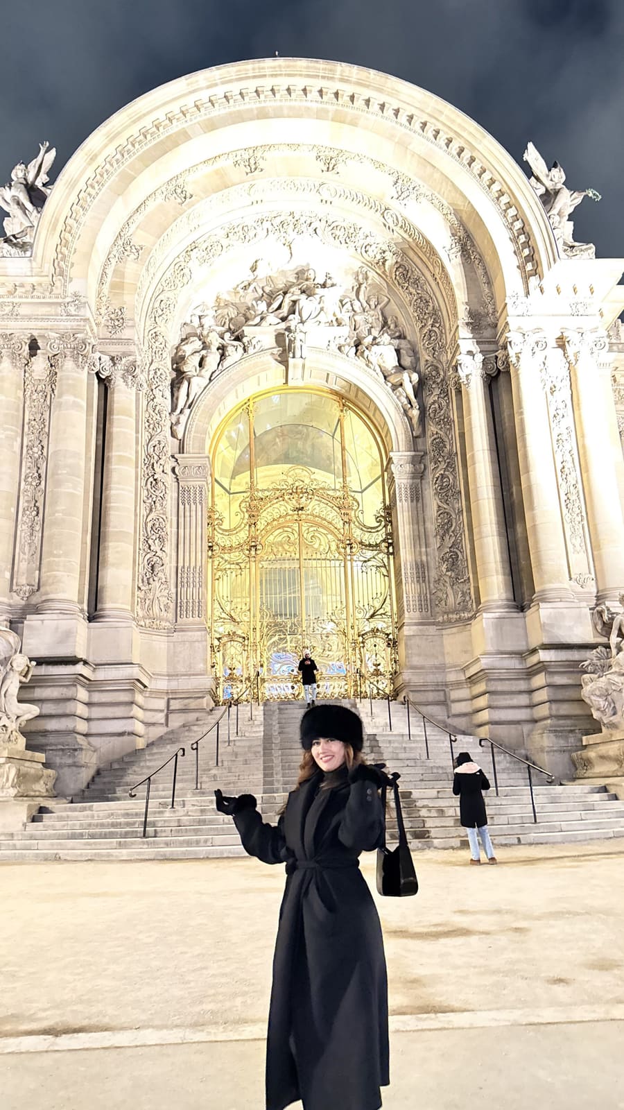 Onesy Carranza con abrigo largo negro y gorro de pelo frente al Petit Palais iluminado de noche