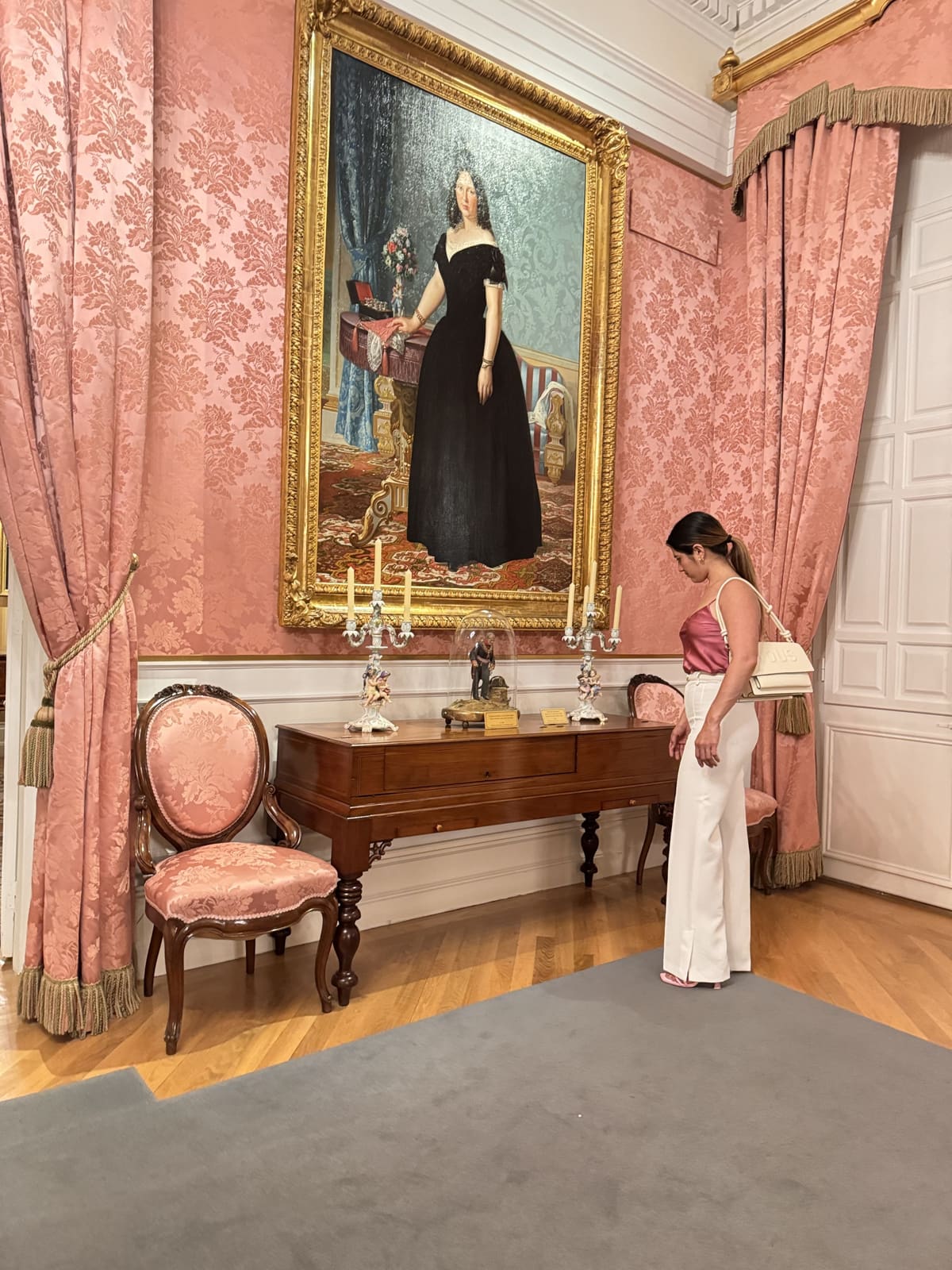 Onesy Carranza con top de satén rosa y pantalón blanco junto a un retrato clásico en una sala de museo